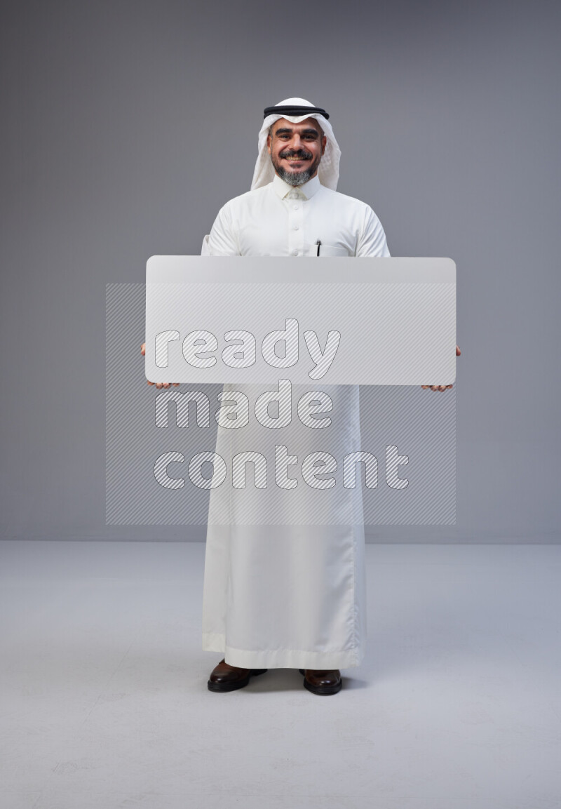 Saudi man Wearing Thob and white Shomag standing holding board on Gray background