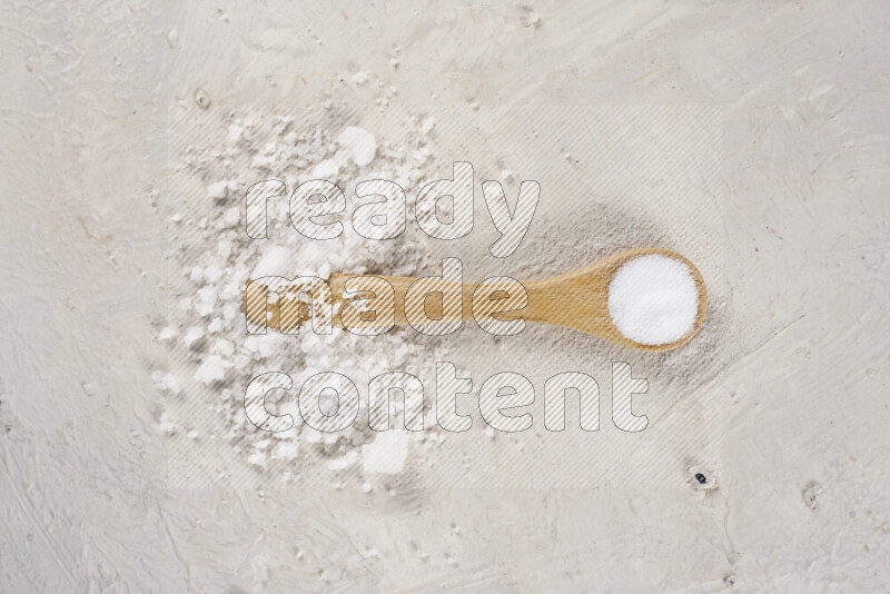 A wooden spoon full of white salt on white background