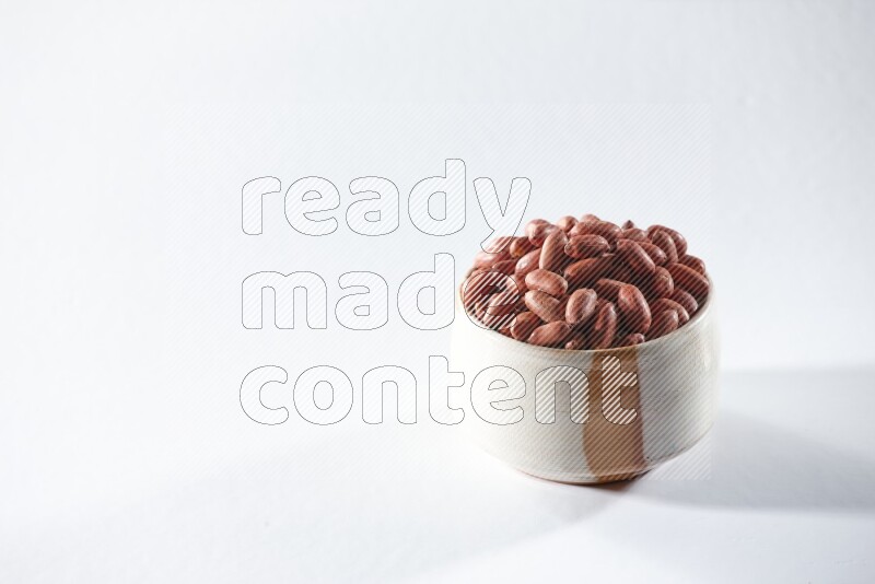 A beige ceramic bowl full of red skin peanuts on a white background in different angles