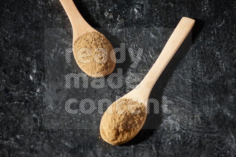 Wooden spoons full of allspice powder on a textured black flooring