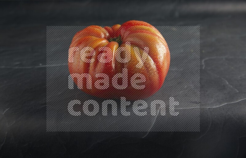 45 degree single heirloom tomato on a textured black slate background
