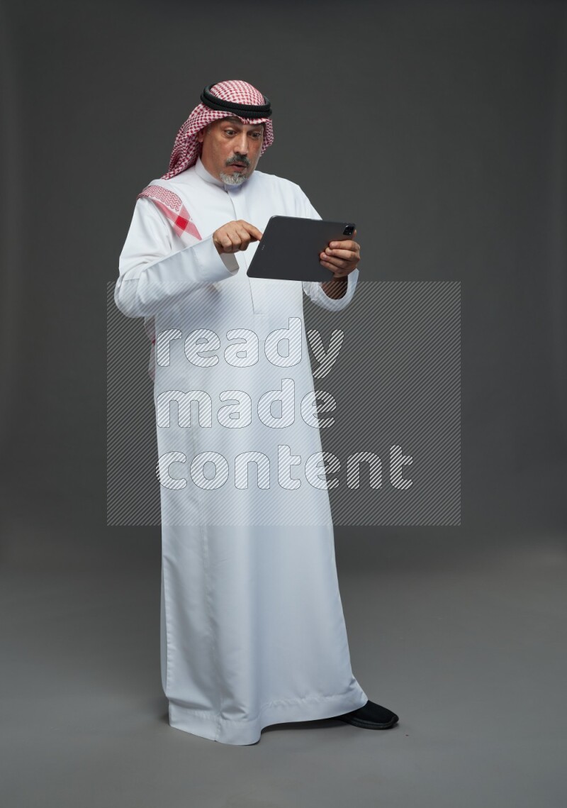 Saudi man with shomag Standing working on tablet on gray background