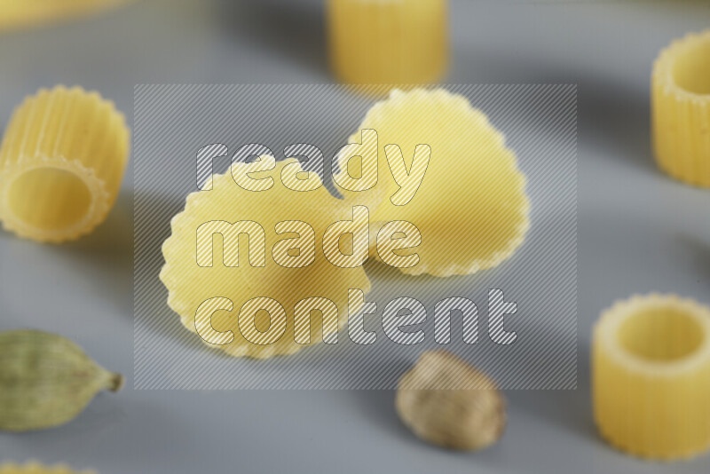 Raw pasta with different ingredients such as cherry tomatoes, garlic, onions, red chilis, black pepper, white pepper, bay laurel leaves, rosemary, cardamom and mushrooms on light blue background
