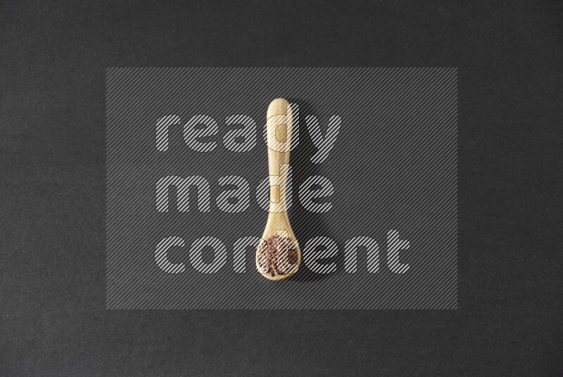 A wooden spoon full of flaxseeds on a black flooring