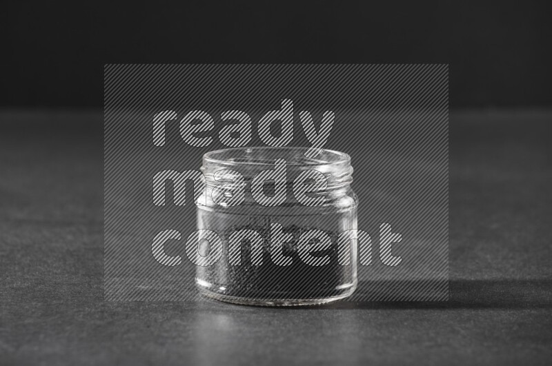 A glass jar full of black seeds on a black flooring