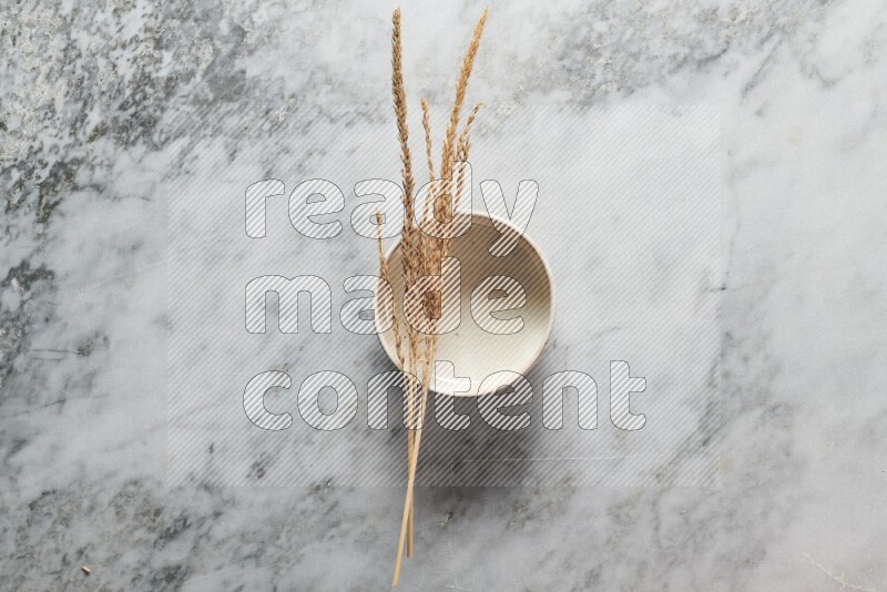 Wheat stalks on beige pottery bowl on grey marble background