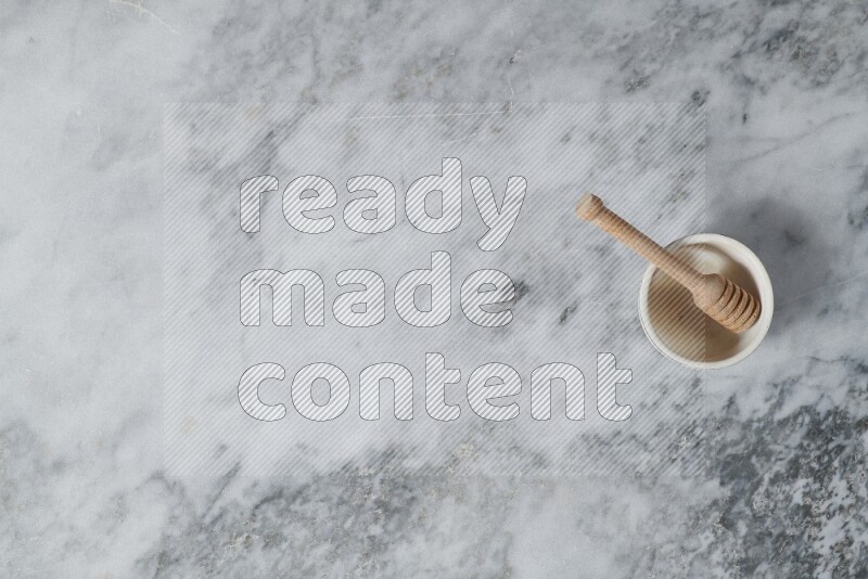 Beige pottery bowl with wooden honey dipper in it on grey marble background