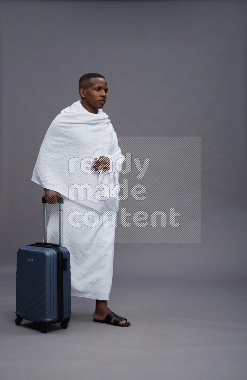 A man wearing Ehram Standing holding traveling bag on gray background