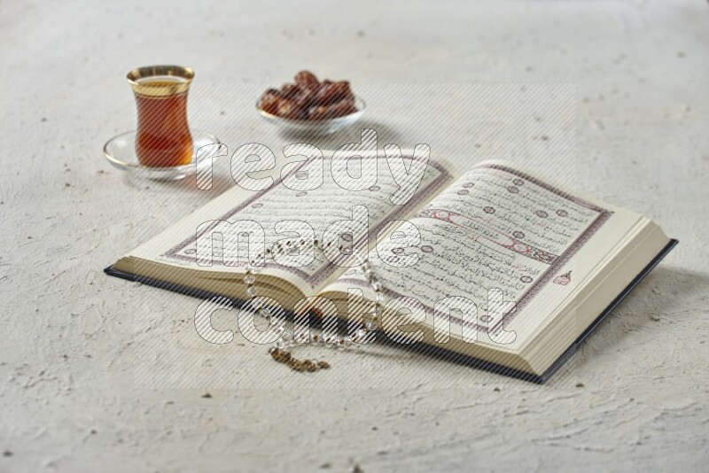 Quran with dates, prayer beads and different drinks all placed on textured white background