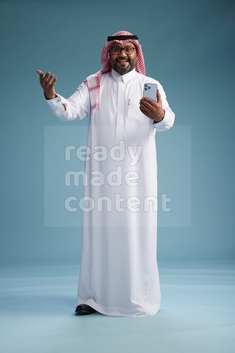 Saudi Man with shimag Standing texting on phone on blue background