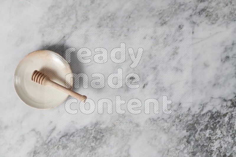 طبق فخاري بيج مع ملعقة عسل خشبية بداخله على خلفية من الرخام الرمادي