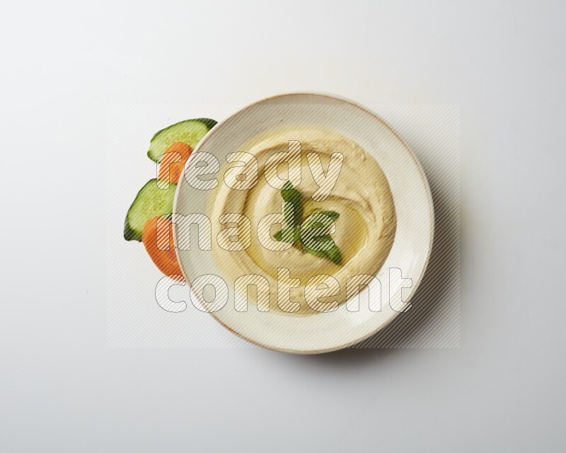 Hummus in a pottry plate garnished with mint  on a white background
