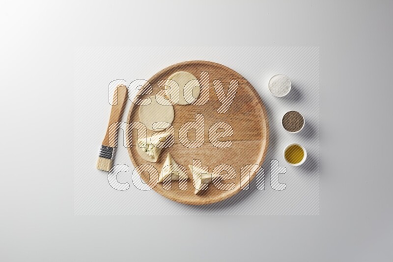 two closed sambosas and one open sambosa filled with cheese while salt, black pepper and oil with oil brush aside in a wooden dish on a white background