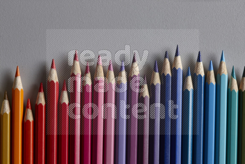 A collection of colored pencils arranged showcasing a gradient of different hues on grey background