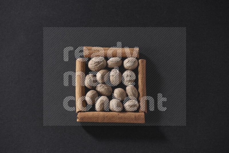 A single square of cinnamon sticks full of nutmeg on black flooring