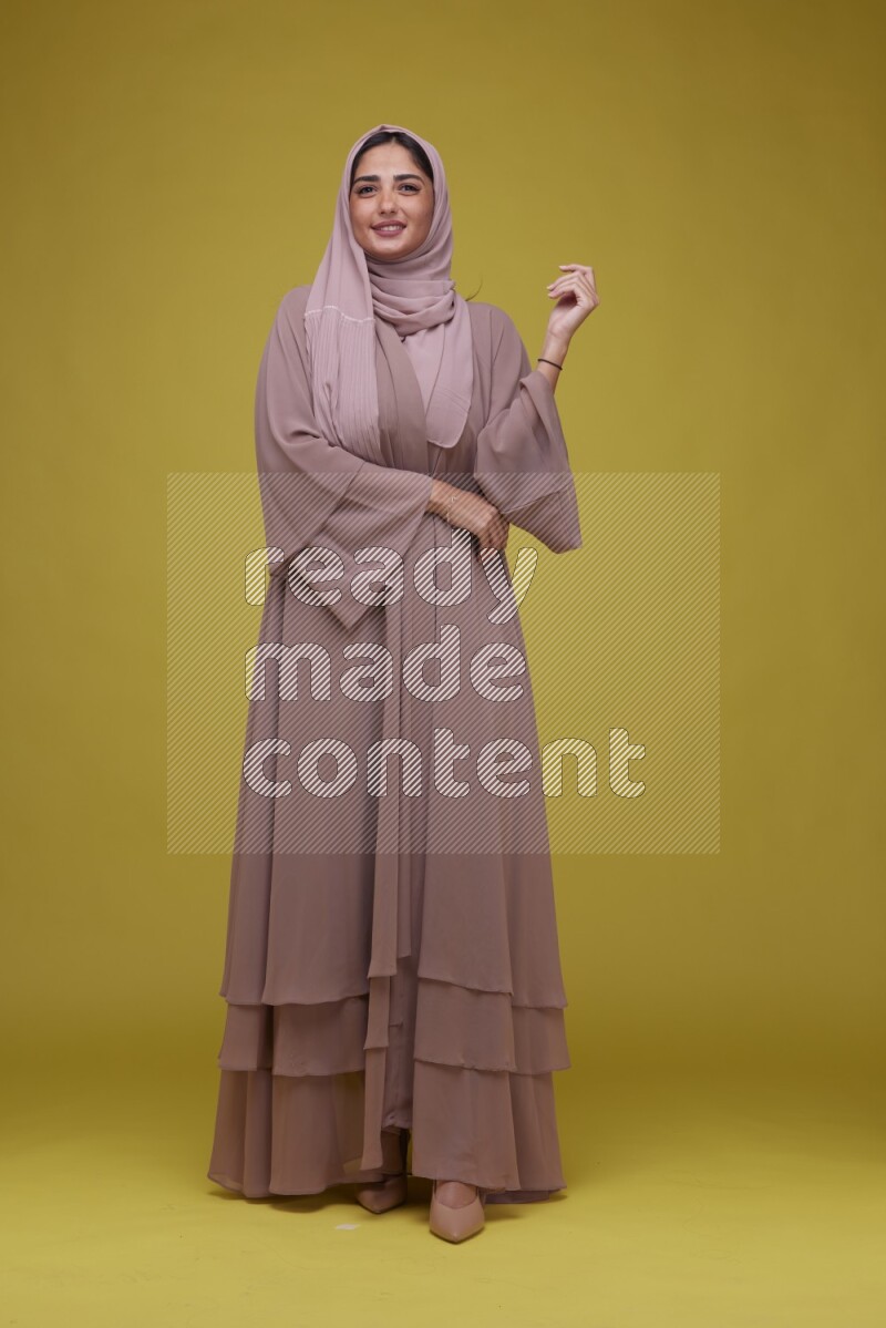 A woman Posing on a Yellow Background wearing Brown Abaya with Hijab