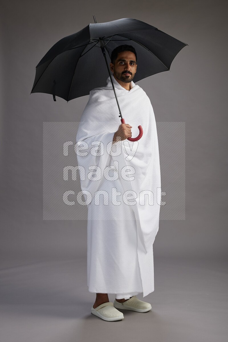 A man wearing Ehram Standing holding umbrella on gray background