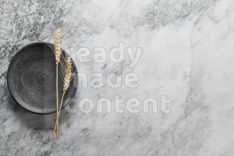 Wheat stalks on black pottery plate on grey marble background