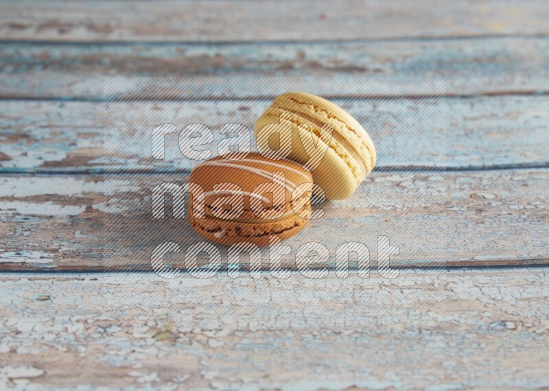 45º Shot of of two assorted Brown Irish Cream, and Yellow Vanilla macarons on light blue background