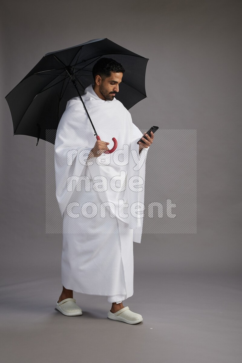 A man wearing Ehram Standing holding umbrella on gray background