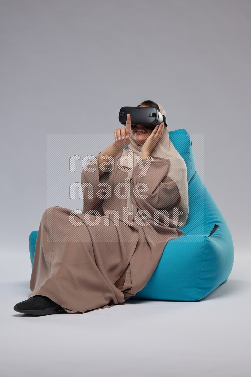 A Saudi woman sitting on a blue beanbag and gaming with VR