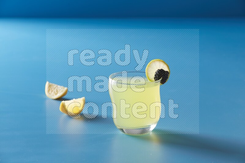 glass of lemon juice with lemon slice and berry on blue background