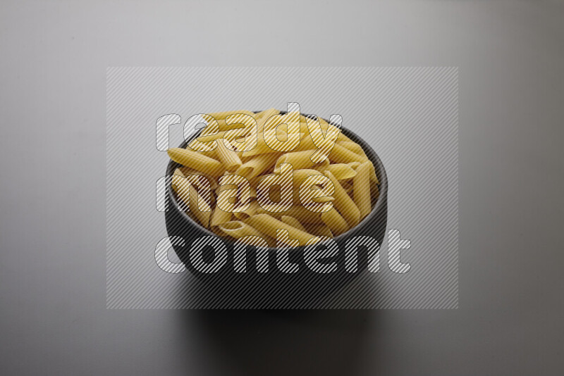 Penne pasta in a pottery bowl on grey background