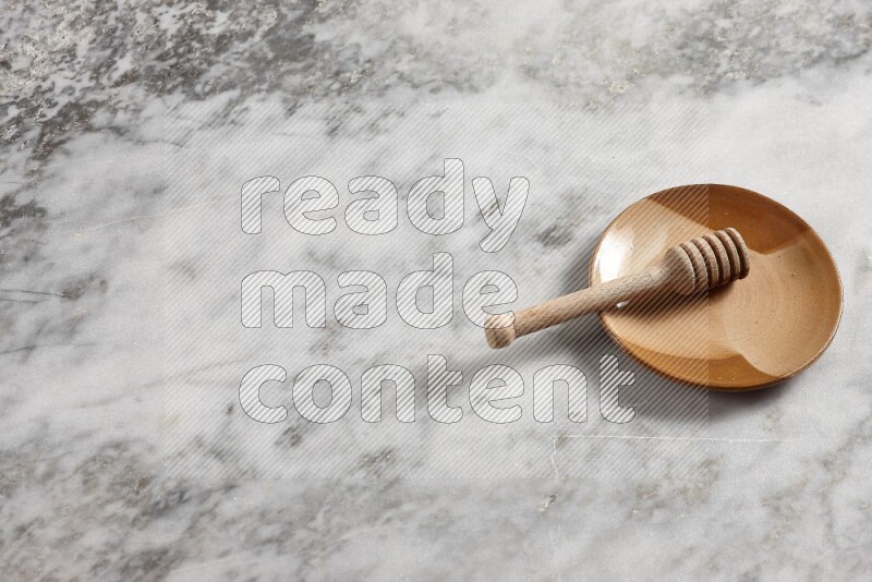 Multicolored pottery plate with wooden honey dipper in it on grey marble background