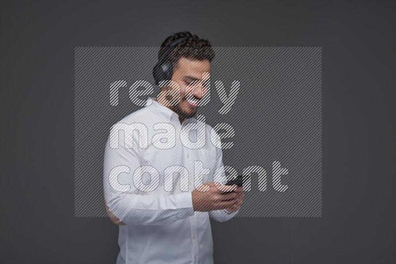 A man wearing smart casual and using his phone and headphone eye level on a gray background