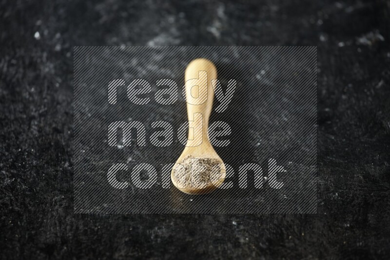 ملعقة خشبية ممتلئة ببودرة الهيل على خلفية سوداء