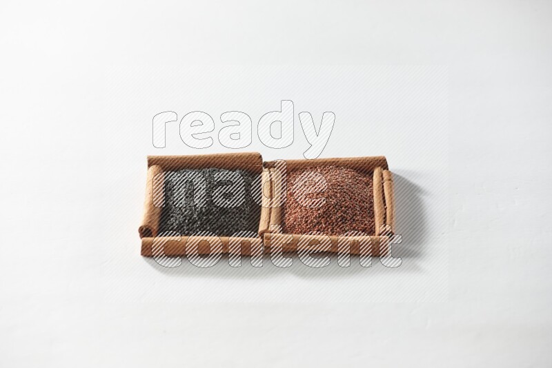 مربعان من أعواد القرفة ممتلئان بحبة البركة السوداء وبذور الكتان علي خلفية بيضاء