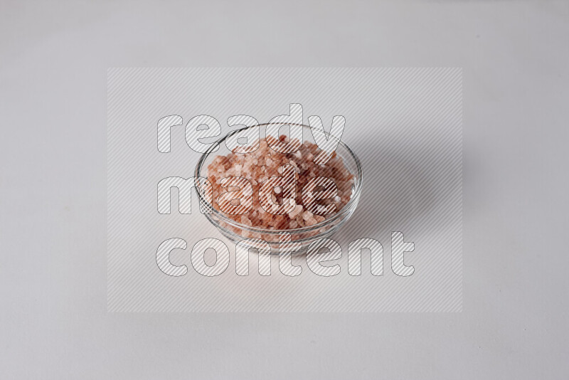 A glass bowl full of coarse himalayan salt crystals on white background