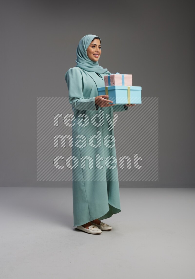 Saudi Woman wearing Abaya standing holding gift box on Gray background