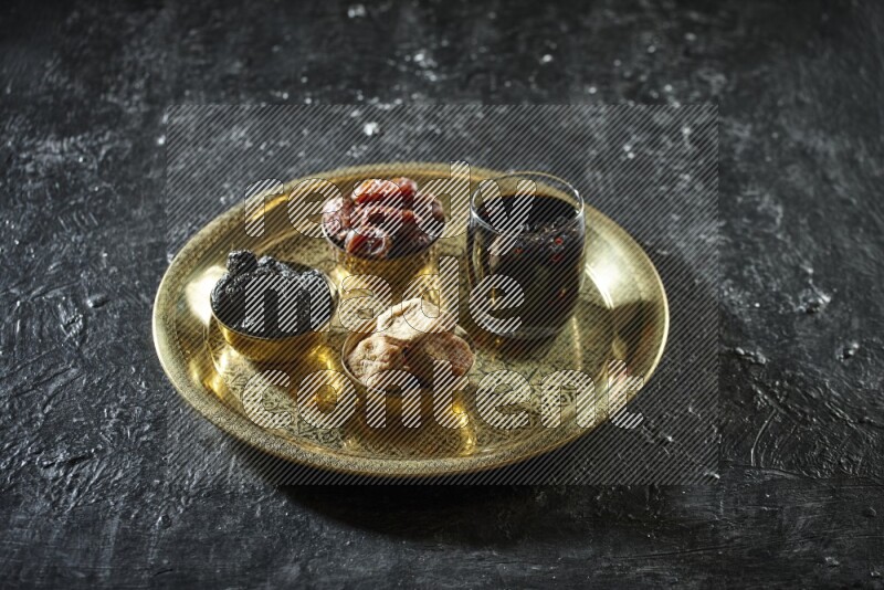 Dried fruits in metal bowls with tamarind on a tray in dark setup