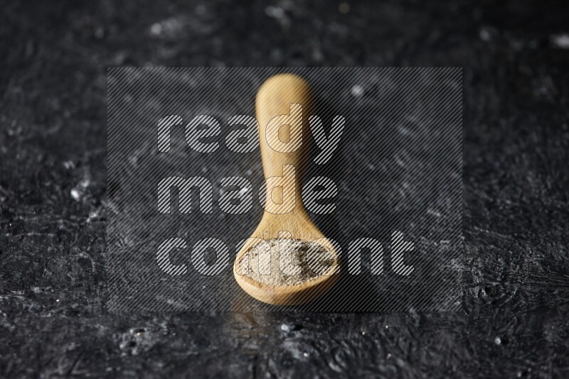 A wooden spoon full of white pepper powder on textured black flooring