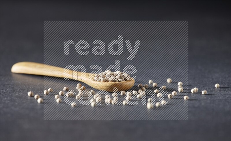 A wooden spoon full of white pepper beads on black flooring