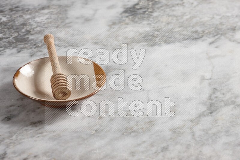 Multicolored pottery plate with wooden honey dipper in it on grey marble background