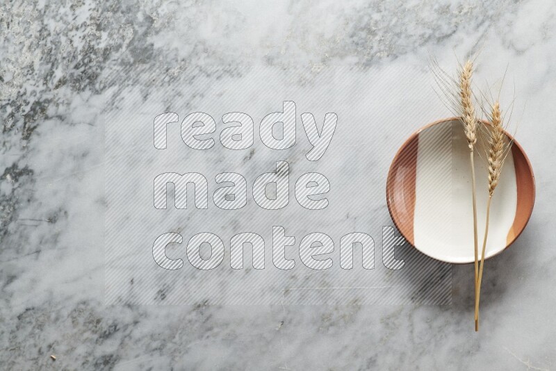 Wheat stalks on multicolored pottery plate on grey marble background