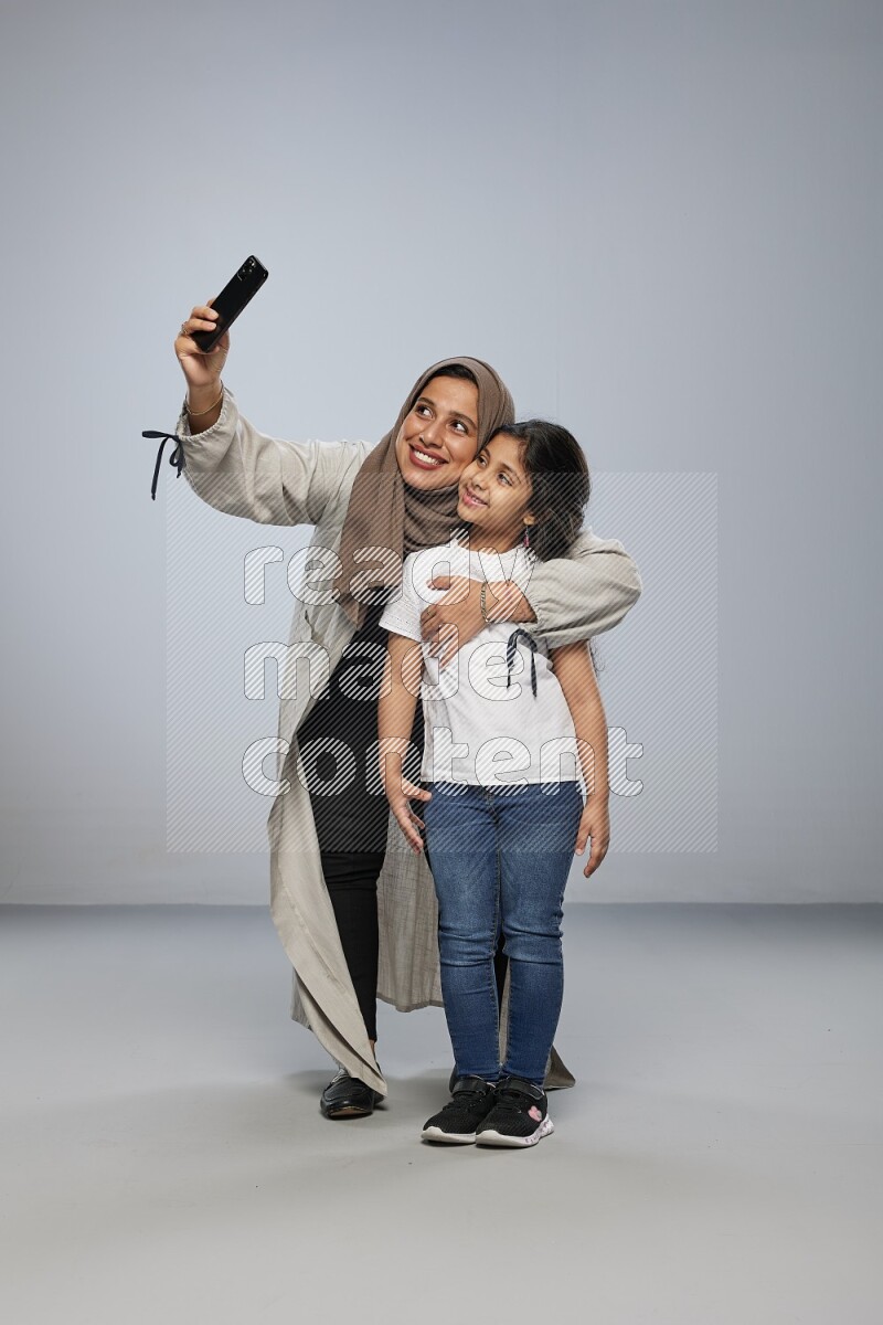 A girl standing taking selfie with her mother on gray background