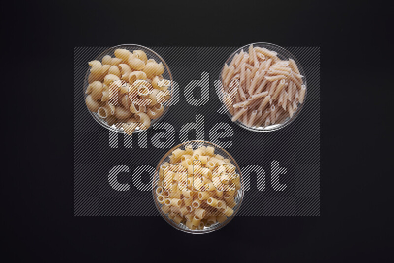Different pasta types in glass bowls on black background