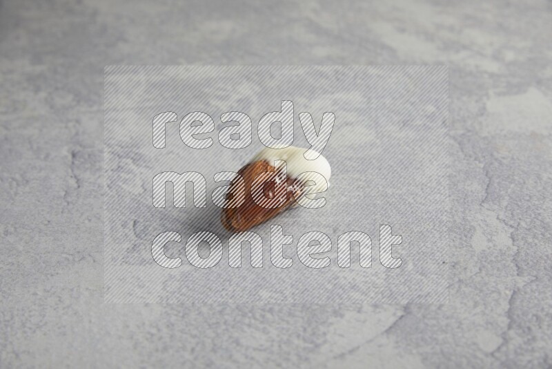 Almond stuffed date coved with white chocolate on a light grey background