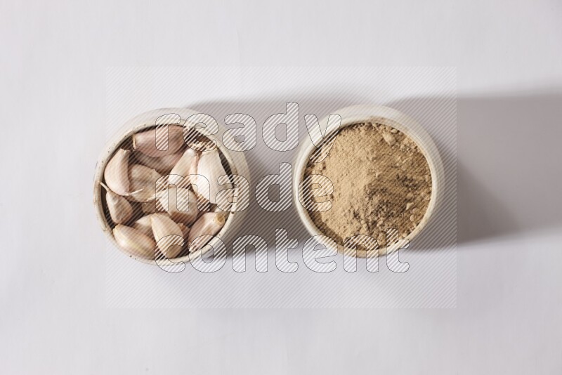 2 beige pottery bowls, one full of garlic powder and the other full of garlic cloves on a white flooring