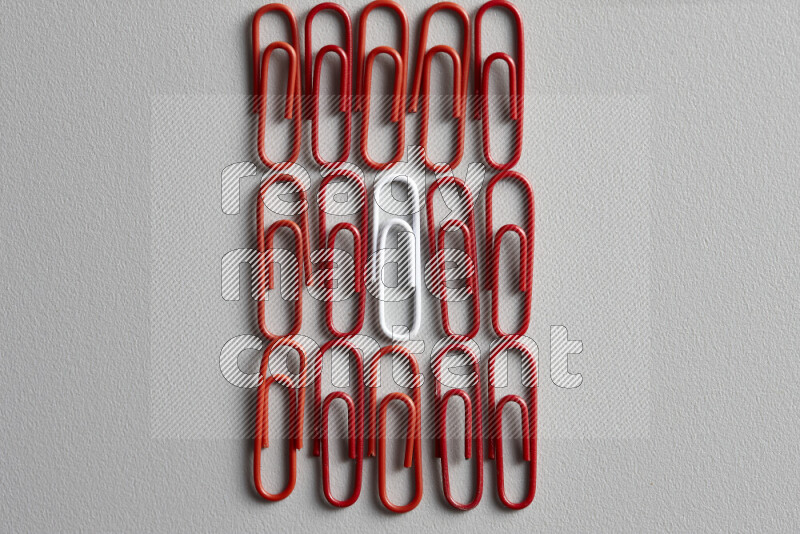 A bunch of red paper clips with a different colored paper clip in the center on grey background