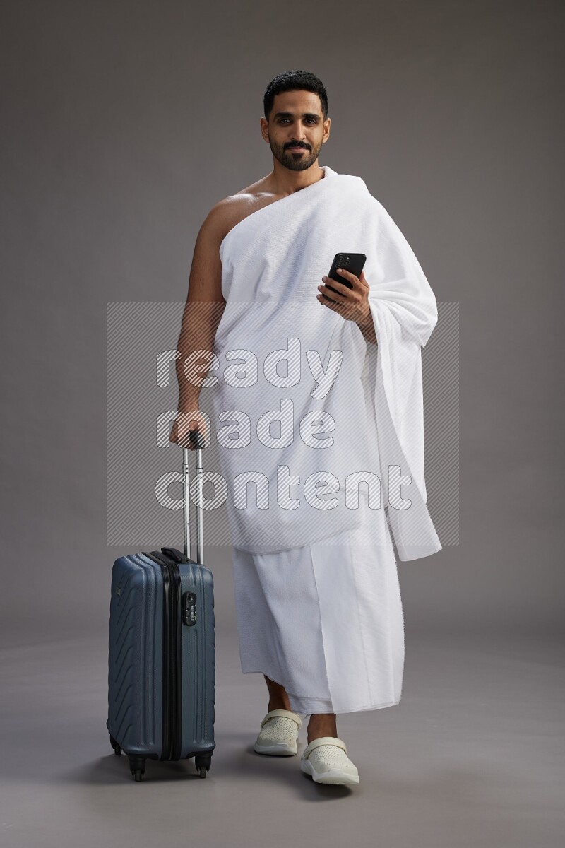 A man wearing Ehram Standing holding traveling bag on gray background