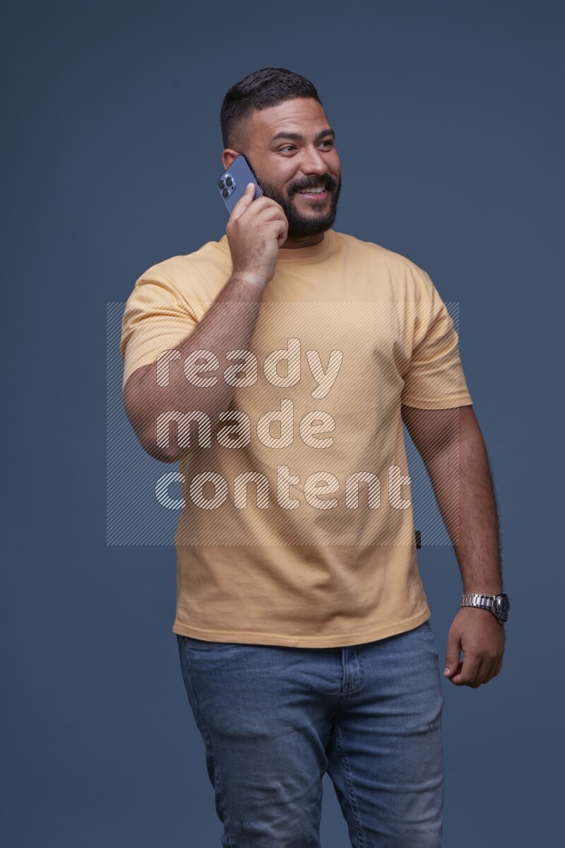 رجل يرتدي بنطال ازرق جينز وقميص اصفر بأكمام قصيره يتحدث بجواله