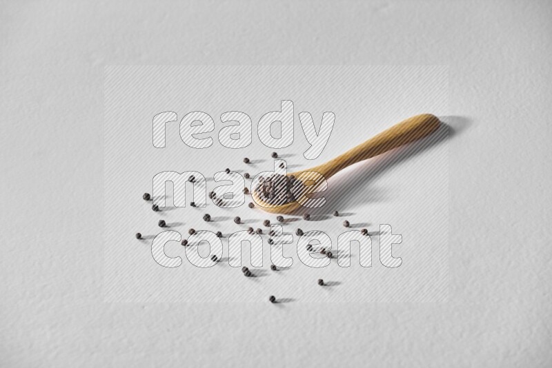 A wooden spoon full of black pepper on white flooring
