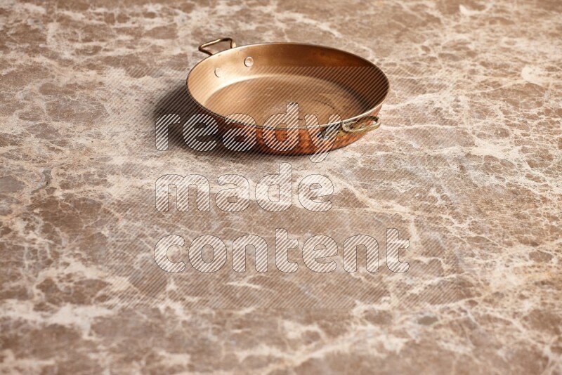 A small copper pan on beige marble background