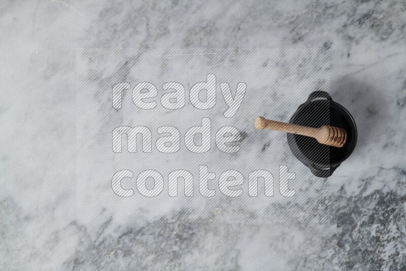 Black pottery bowl with wooden honey dipper in it on grey marble background
