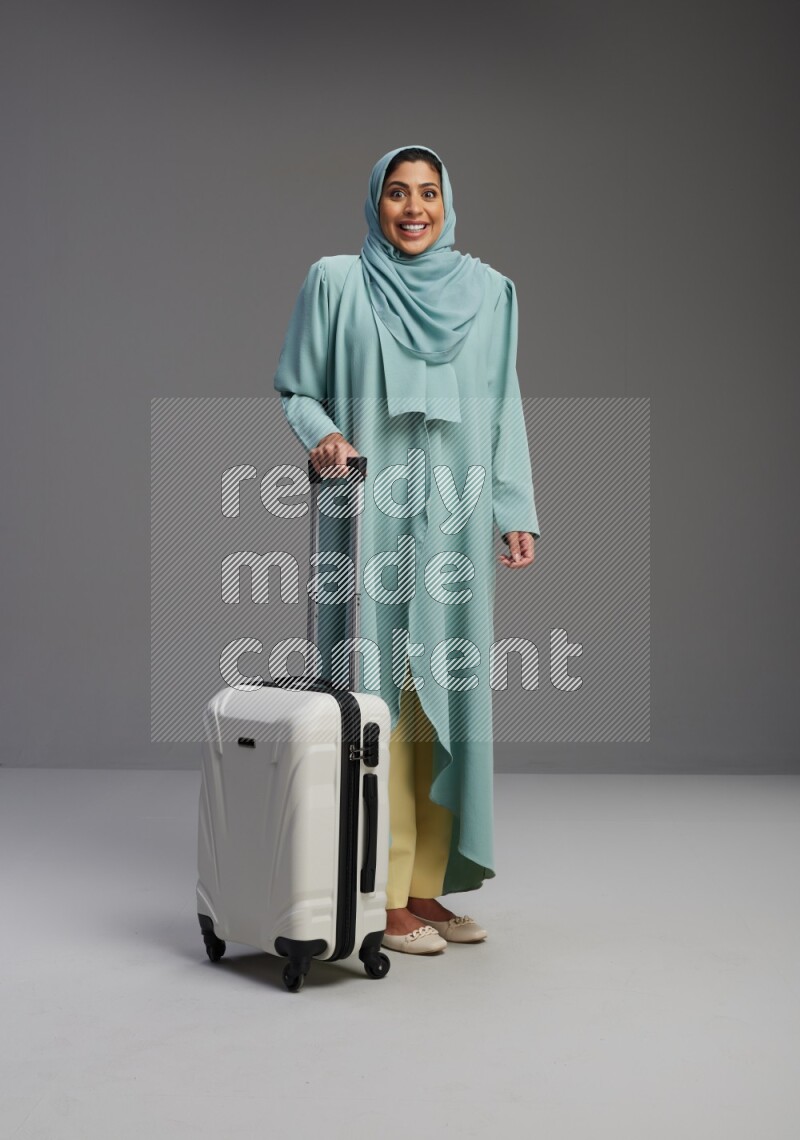Saudi Woman wearing Abaya standing holding Travel bag on Gray background