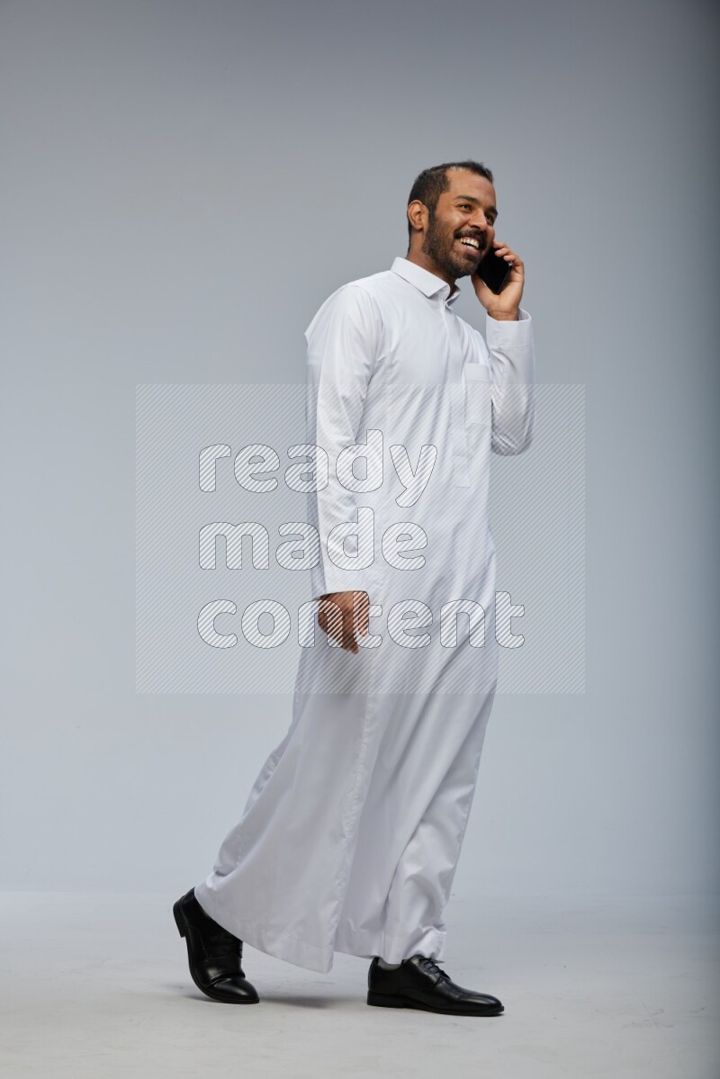 Saudi man wearing Thob standing talking on phone on Gray background